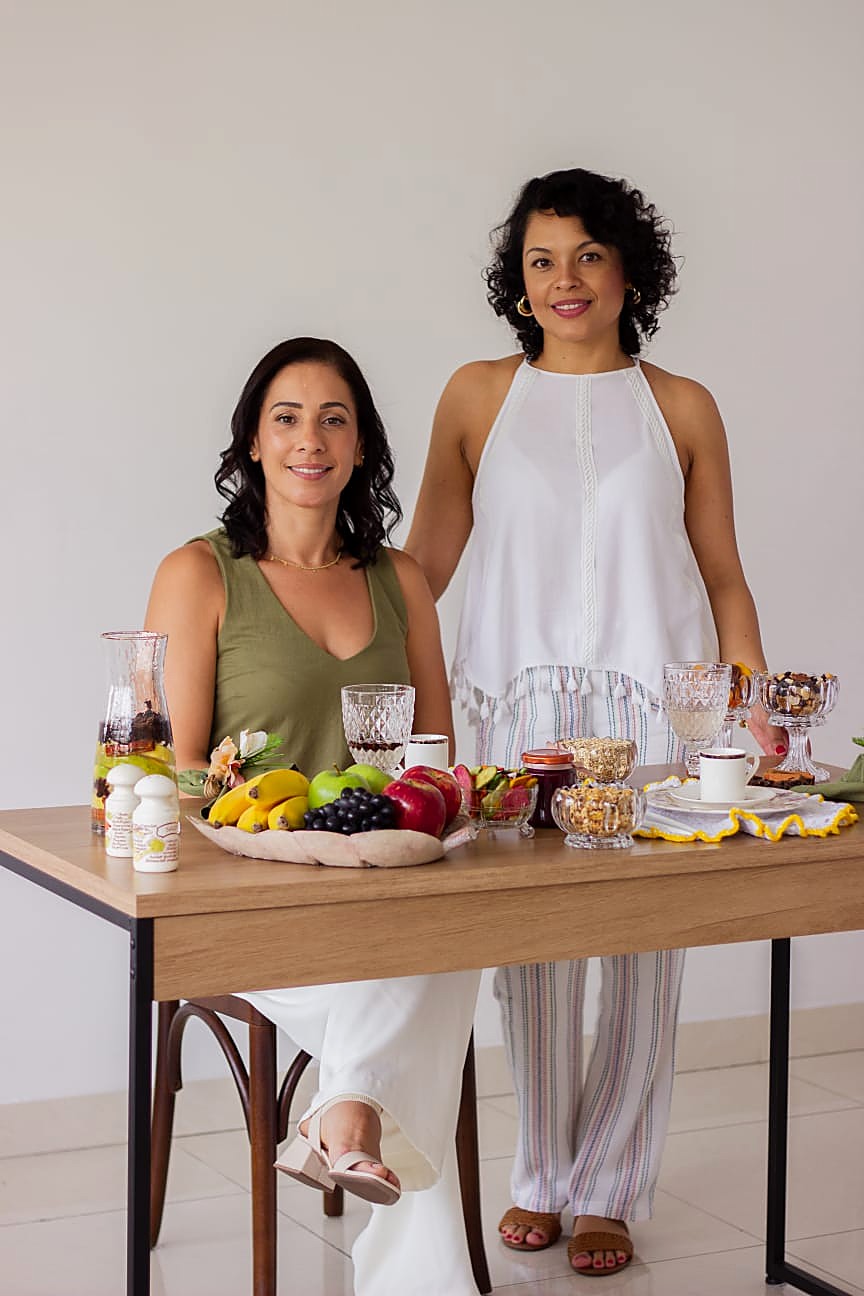 Deise e Paula, fundadoras da Casa Dela Empório, em mesa com produtos naturais